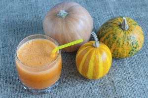 Healthy Pumpkin Spice Smoothie and three different pumpkins on sackcloth surface.